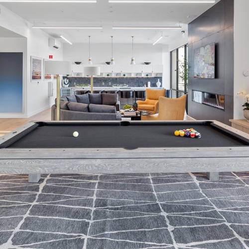 Clubhouse Dog Friendly Apartments in Tracy CA - The Vela - Clubhouse with Couches, Chairs, an Electric Fireplace, a Pool Table, a Communal Kitchen, and Expansive Windows